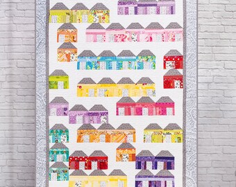 May include: A colourful quilt featuring a pattern of houses with different coloured roofs and windows. The houses are arranged in a staggered pattern, creating a dynamic and playful design.