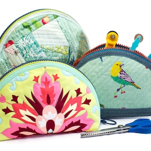 May include: Three half-circle zippered pouches with different fabric patterns. The pouches are made of quilted fabric and have a light blue, green, and yellow color scheme. The pouch on the left has a floral pattern in shades of pink, red, and white. The pouch in the middle has a bird pattern in shades of yellow, green, and blue. The pouch on the right has a patchwork pattern in shades of green, white, and red. A pair of blue fabric scissors is in the foreground.