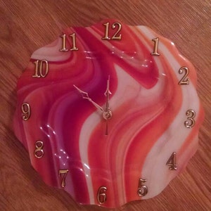 May include: A red, white, and pink swirl clock with gold numbers. The clock face is shaped like a flower.