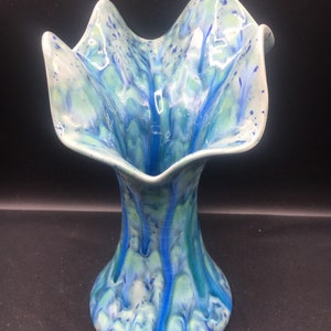 May include: A blue and green ceramic vase with a wide, ruffled opening and a narrow base. The vase has a unique, marbled glaze with streaks of blue and green.