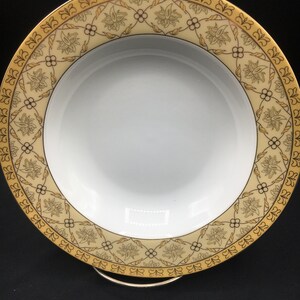 May include: A white ceramic soup bowl with a gold and brown floral pattern around the rim.