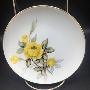 May include: A white porcelain plate with a gold rim features a yellow rose with gray leaves and a white background.