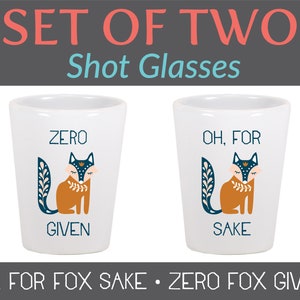 May include: Set of two white ceramic shot glasses with fox illustrations and text. One glass says "Zero Fox Given" and the other says "Oh, For Fox Sake".