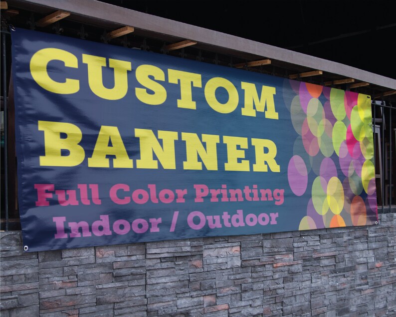 May include: A blue banner with the text "CUSTOM BANNER" in yellow letters. The banner also says "Full Color Printing Indoor/Outdoor" in pink and white letters. The banner has a colorful background of overlapping circles.