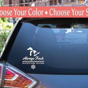 May include: A white vinyl decal on a car window. The decal features a stylized outline of the Great Lakes, with the text "Always Fresh, Sometimes Frozen" and a snowflake graphic. The top of the window has the text "Choose Your Color • Choose Your Size".