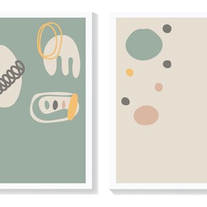 May include: Two framed abstract art prints with a minimalist design. The print on the left has a light green background with white, yellow, and black abstract shapes. The print on the right has a light beige background with various sized circles in shades of green, pink, yellow, and black.