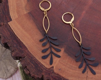 May include: A pair of gold and black dangle earrings with a leaf design. The earrings are made of metal and have a delicate, feminine look.