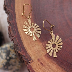 Può includere: Un paio di orecchini dorati con un design a forma di sole. Gli orecchini sono realizzati in metallo martellato e hanno un'apertura circolare al centro.