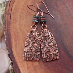 May include: Copper earrings with a filigree design and green and brown gemstone accents.