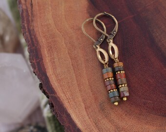 Peut inclure: Une paire de boucles d'oreilles pendantes avec un design de perles empilées. Les boucles d'oreilles présentent des fermoirs à levier et des accents ovales de couleur or. Les perles sont dans des tons de rouge, marron, bleu et or.