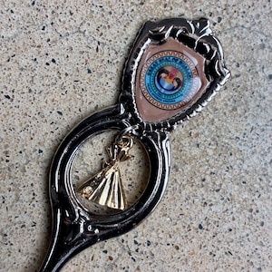 Peut inclure: Une cuillère souvenir en métal argenté avec un emblème en forme de bouclier au sommet portant le Grand Sceau de la tribu Hualapai de l'Arizona. Une petite breloque en forme de cloche dorée pend dans une ouverture circulaire du manche.