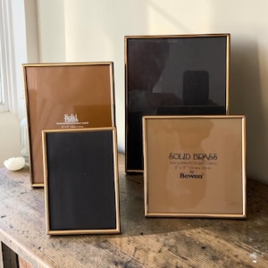 Puede incluir: Una colección de cuatro marcos de fotos de latón macizo, rectangulares y cuadrados, con bordes metálicos finos. Los marcos cuentan con frentes de vidrio transparente e insertos de papel con el texto Solid Brass, hand polished & lacquer coated.