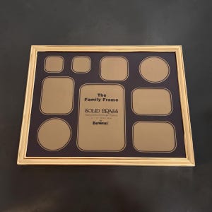 May include: A rectangular solid brass multi-opening picture frame with a polished gold finish. The dark mat features eight varied openings for photos and text that reads: The Family Frame, SOLID BRASS, 28 cm by 36 cm, by Bowon.