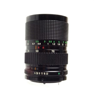 May include: A black camera lens with a green and white aperture ring. The lens has a focal length of 35-70mm and an aperture of f/4-22. The lens also has a depth of field scale and a focus ring.