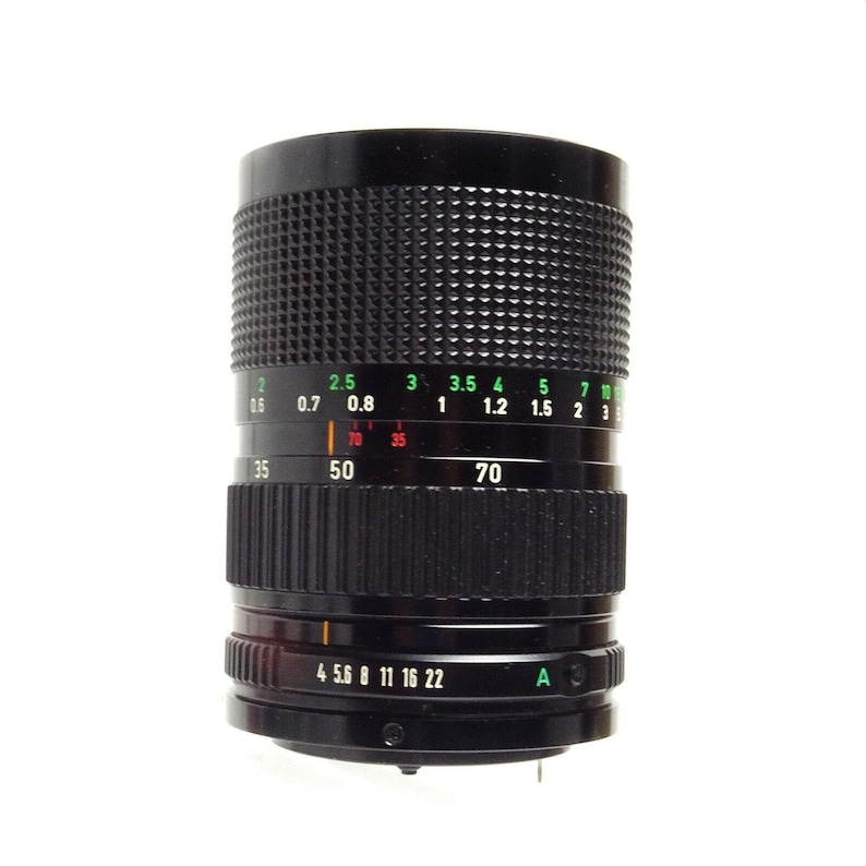 May include: A black camera lens with a green and white aperture ring. The lens has a focal length of 35-70mm and an aperture of f/4-22. The lens also has a depth of field scale and a focus ring.