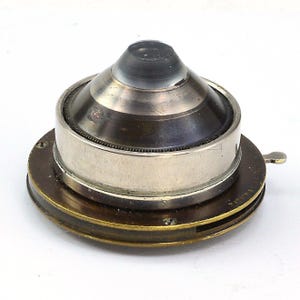 May include: A vintage brass and silver camera lens with a glass element. The lens is mounted on a brass base with a rotating mechanism.