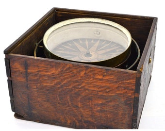 Puede incluir: Una brújula de latón vintage en una caja de madera. La brújula tiene una cubierta de vidrio y una rosa de los vientos en blanco y negro.