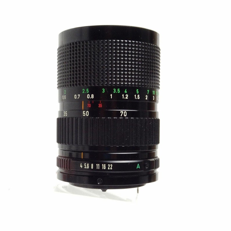 May include: A black camera lens with a green and white aperture ring. The ring has markings for f-stops from 0.6 to 10 and focal lengths from 35 to 70. The lens also has a black ring with markings for aperture settings from 4 to 22.