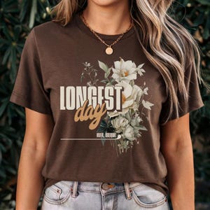 May include: Brown t-shirt with a floral design and the text "LONGEST day" in a vintage style font. The text "HVER ISELDUR" is printed below the floral design.