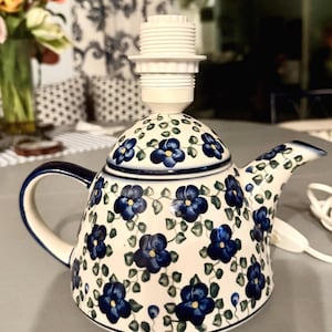 Könnte beinhalten: Keramik-Teekannen-Lampensockel mit weißem Hintergrund und blauem Blumenmuster. Die Teekanne hat einen dunkelblauen Griff und Ausguss, und eine weiße Lampenfassung ist oben angebracht. Die Lampe ist als dekorative Leuchte konzipiert.