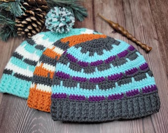 May include: Three crocheted hats in different color patterns. The hats are made with a variety of colors, including teal, orange, white, gray, and purple. The hats are stacked on top of each other.