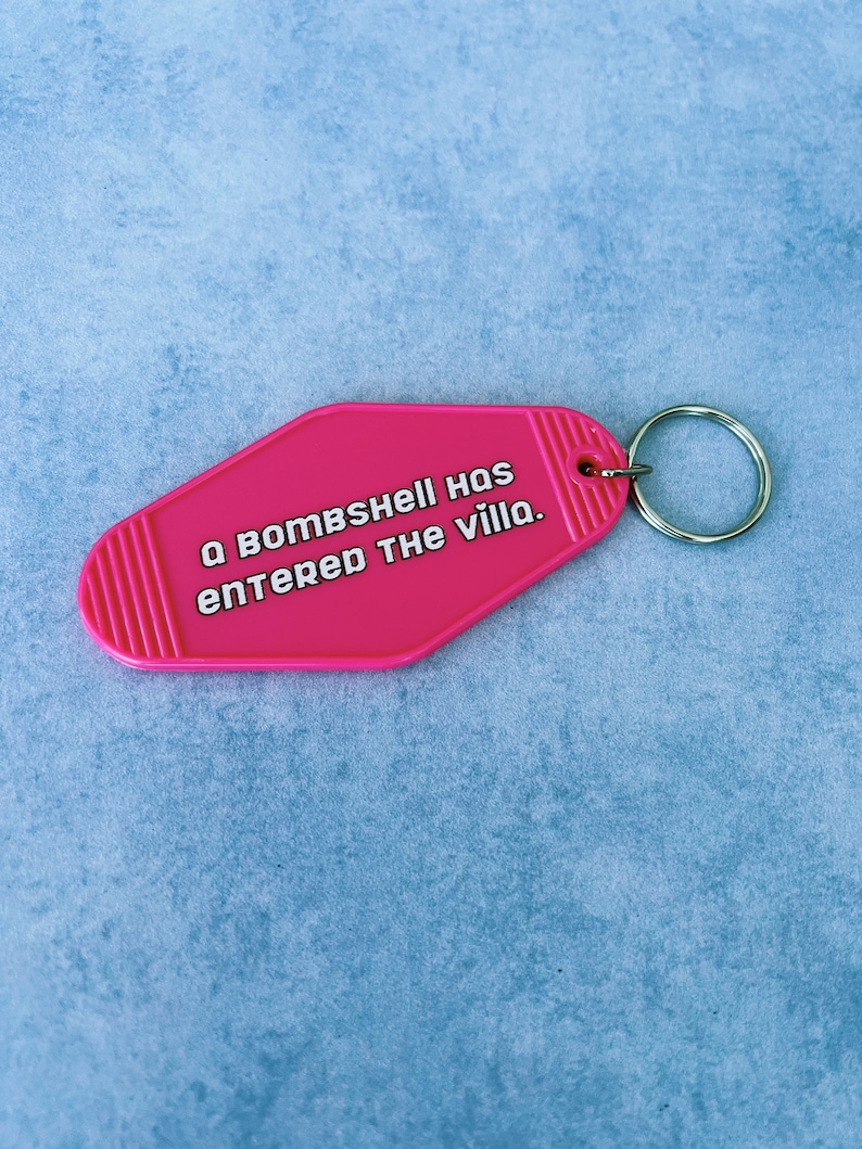 May include: A pink motel key chain with the text "A bombshell has entered the villa."