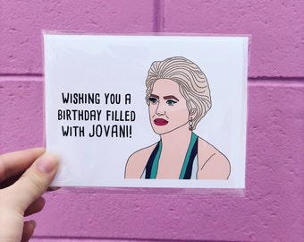 Puede incluir: Una tarjeta blanca con una ilustración de dibujos animados de una mujer con cabello rubio y un vestido verde y azul. El texto en la tarjeta dice "Wishing you a birthday filled with Jovani!"