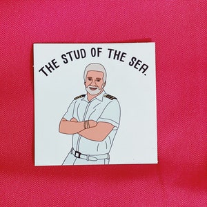 Op de afbeelding: Een witte sticker met een cartoonillustratie van een man met een witte baard en snor, die een wit uniform met een gouden streep draagt. De tekst "THE STUD OF THE SEA." staat boven de man.