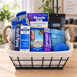 May include: A wire basket with a fabric liner containing a pair of gray socks with a blue ribbon, a Body Glide anti-chafe balm, a Muscle Rub packet, a Clif Bar, a Propel grape electrolyte powder packet, Muscle Rehab bath soak, and a blue ball.