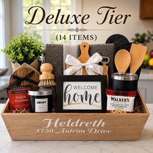May include: A wooden gift basket labeled Heldreth 4750 Antrim Drive containing 14 items including a Welcome Home sign, a DKNY candle, Stash English Breakfast tea, Walker's shortbread, a small potted plant, wooden utensils, a cutting board, and a towel.