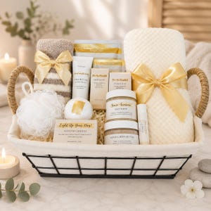 May include: A gift basket with a black wire frame and rope handles containing a beige striped towel, a white waffle-weave towel, both with gold ribbons, a white bath pouf, a candle, hand cream, massage oil, soap, salt scrub, and body butter.