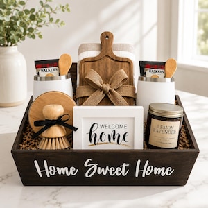 May include: A dark wooden gift crate labeled Home Sweet Home containing a wooden cutting board with a burlap bow, two white tumblers with Walker's shortbread, a wooden scrub brush, a white sign reading Welcome home, and a Lemon Lavender soy candle.