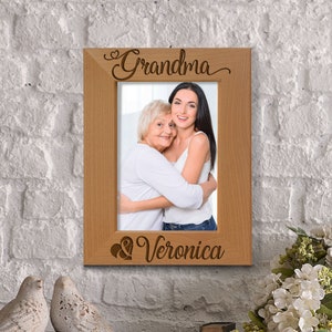 May include: A wooden picture frame with the words "Grandma & Veronica" engraved on it. The frame holds a photo of two women, one older and one younger, hugging each other.