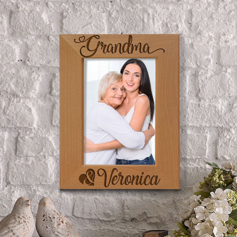 May include: A wooden picture frame with the words "Grandma & Veronica" engraved on it. The frame holds a photo of two women, one older and one younger, hugging each other.