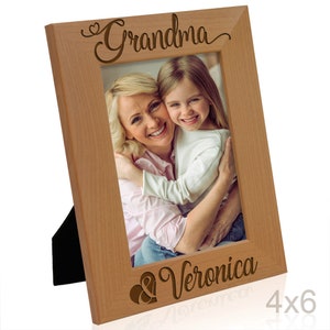 May include: A wooden picture frame with a light brown finish. The frame has a heart and the word "Grandma" engraved on the top and the word "Veronica" engraved on the bottom. The frame is holding a photo of a woman and a young girl.