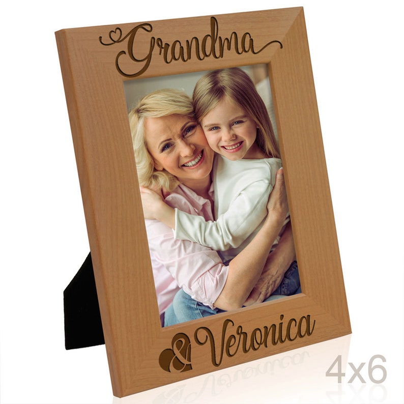 May include: A wooden picture frame with a light brown finish. The frame has a heart and the word "Grandma" engraved on the top and the word "Veronica" engraved on the bottom. The frame is holding a photo of a woman and a young girl.