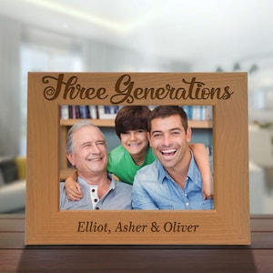 May include: A wooden photo frame with the text "Three Generations" engraved on the top. The frame has a photo of three generations of a family, with the names "Elliot, Asher & Oliver" engraved below the photo.