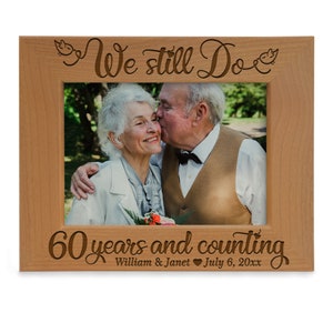 May include: A wooden photo frame with the text "We still do 60 years and counting William & Janet July 6, 20xx" engraved on the front. The frame has a picture of an older couple in it.