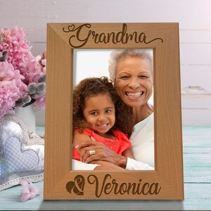 May include: A wooden picture frame with a heart and the words "Grandma & Veronica" engraved on it. A photo of a grandmother and granddaughter is in the frame.