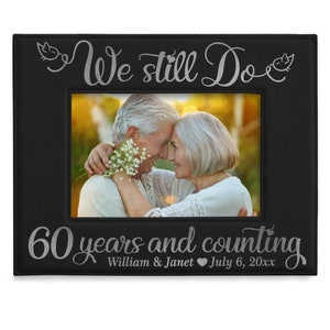 May include: Black leather picture frame with a silver inscription that reads "We still do 60 years and counting William & Janet July 6, 20xx". The frame has a photo of an older couple embracing.
