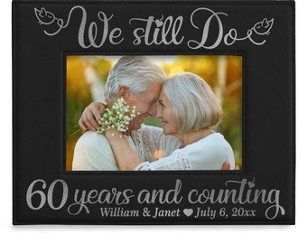 Może przedstawiać: Czarna skórzana ramka na zdjęcia z srebrnym napisem "We still do 60 years and counting William & Janet July 6, 20xx". W ramce znajduje się zdjęcie starszej pary, która się obejmuje.