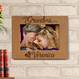 May include: A wooden picture frame with the words "Grandma & Veronica" engraved on it. The frame has a photo of an older woman and a young girl.