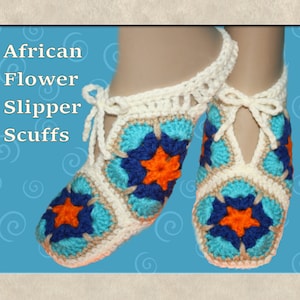 Op de afbeelding: Gehaakte pantoffels met een witte basis en een kleurrijk Afrikaans bloemenpatroon in tinten blauw, oranje en bruin. De pantoffels hebben een strik aan de enkel.