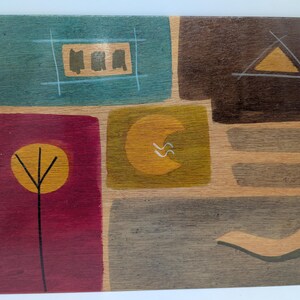 May include: Abstract wooden artwork with a patchwork design. The piece features geometric shapes in teal, brown, burgundy, and gold. A tree-like shape and a crescent moon are also depicted. The artwork is signed in the bottom right corner.