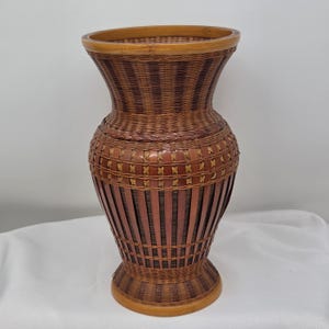 May include: A tall, woven bamboo vase featuring a flared rim and a rounded body. The design incorporates alternating vertical strips of dark brown and light tan bamboo, accented by intricate cross-hatched weaving patterns around the midsection.