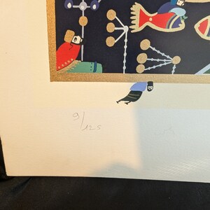 May include: A colorful print with a black background featuring a red bird, a blue and white geometric design, and a gold frame. The print is signed "9/125".