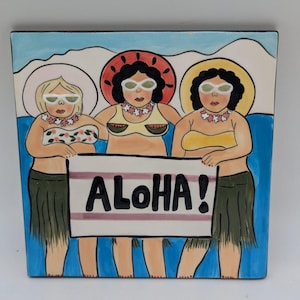 May include: Square ceramic tile featuring three cartoon figures in swimwear and sunglasses, holding a sign that reads "ALOHA!". The figures are set against a blue and white background, evoking a beach scene.