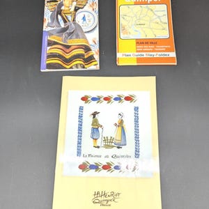 May include: Three printed items: a book titled "Quimper Pottery", a map titled "Quimper", and a postcard with the text "La Faience de Quimper". The items are in various colors, including yellow, orange, blue, and black. The postcard features illustrations of people in traditional Breton attire.