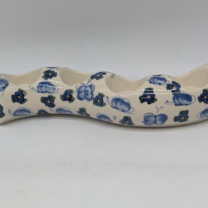 May include: Cream-colored ceramic serving dish with four connected compartments. The dish is decorated with blue floral and butterfly patterns. It has a curved shape and a handle on one end.