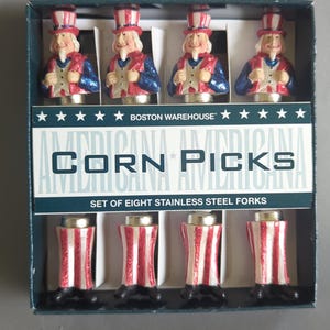 May include: A set of eight stainless steel corn picks in a box labeled Boston Warehouse Americana Corn Picks. The picks feature Uncle Sam figures with red, white, and blue glittered clothing, including top hats, jackets, and striped trousers.